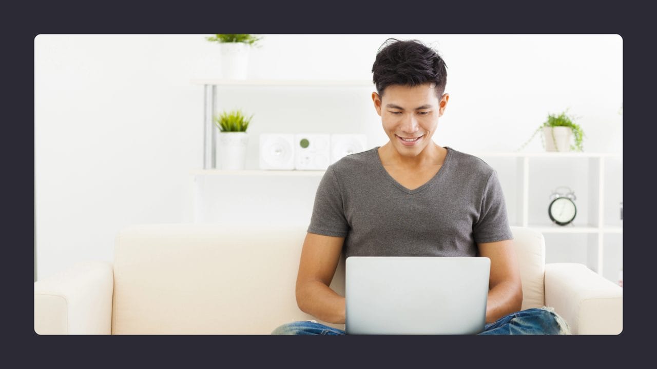 Man smiling while using laptop on sofa