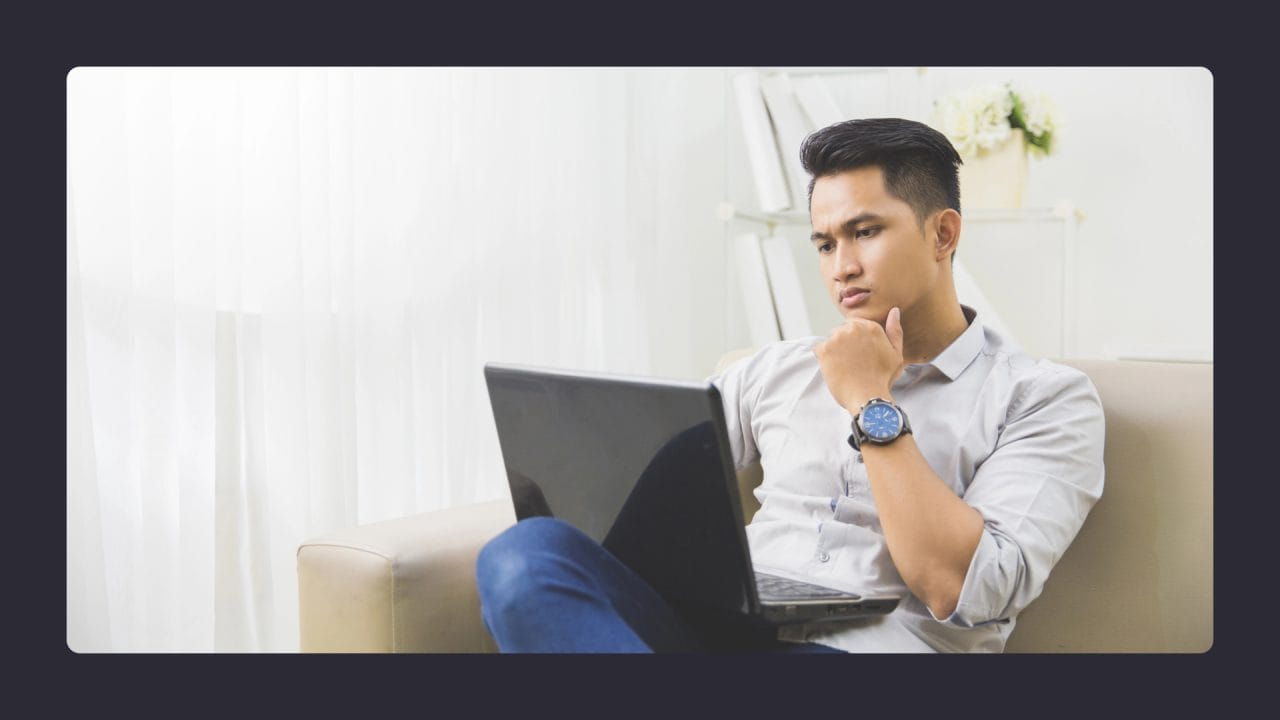 Man pondering while using laptop on sofa