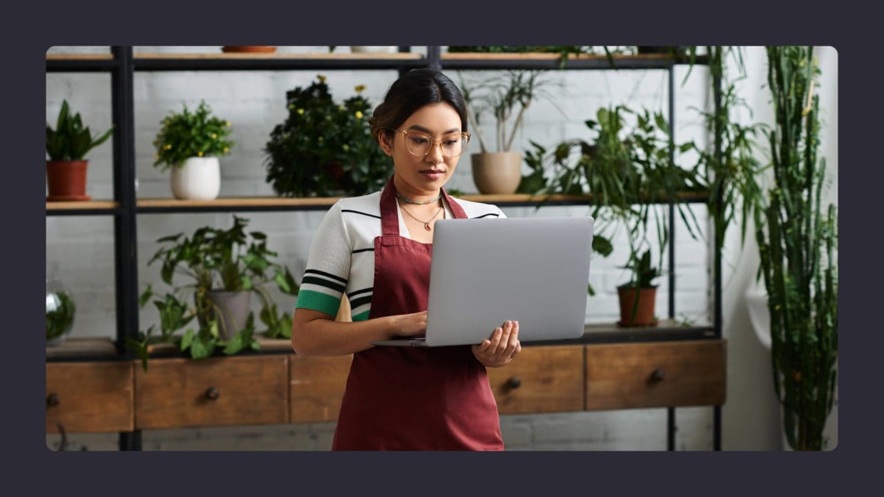 Woman in apron using laptop in plant-filled room