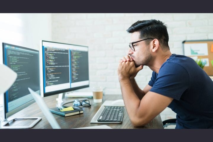 Man analysing code on computer screens in office