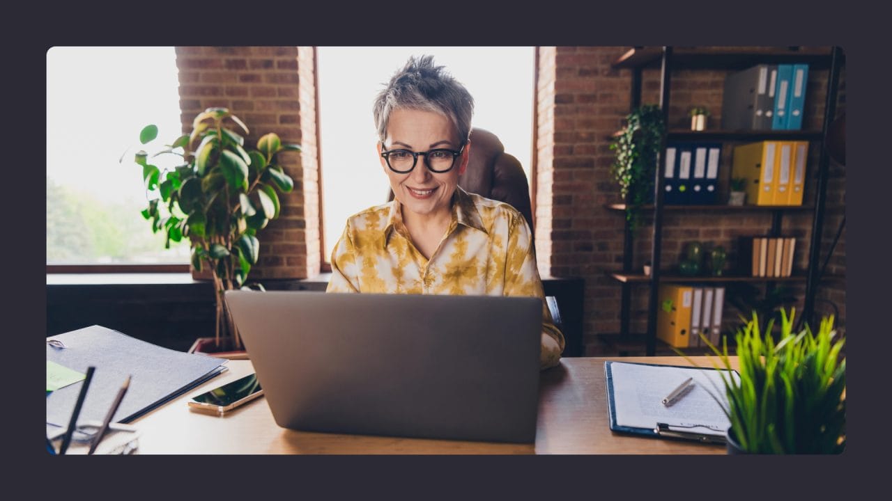 Smiling woman using laptop in sunny office space