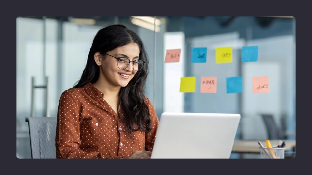 Smiling woman working on laptop with sticky notes