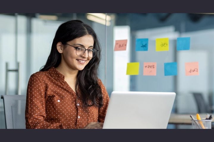 Smiling woman working on laptop with sticky notes