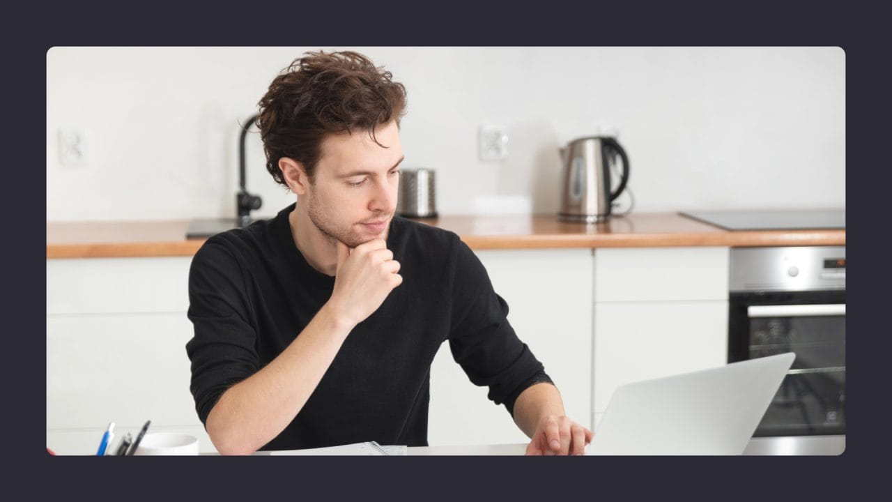 Man pondering at laptop in modern kitchen