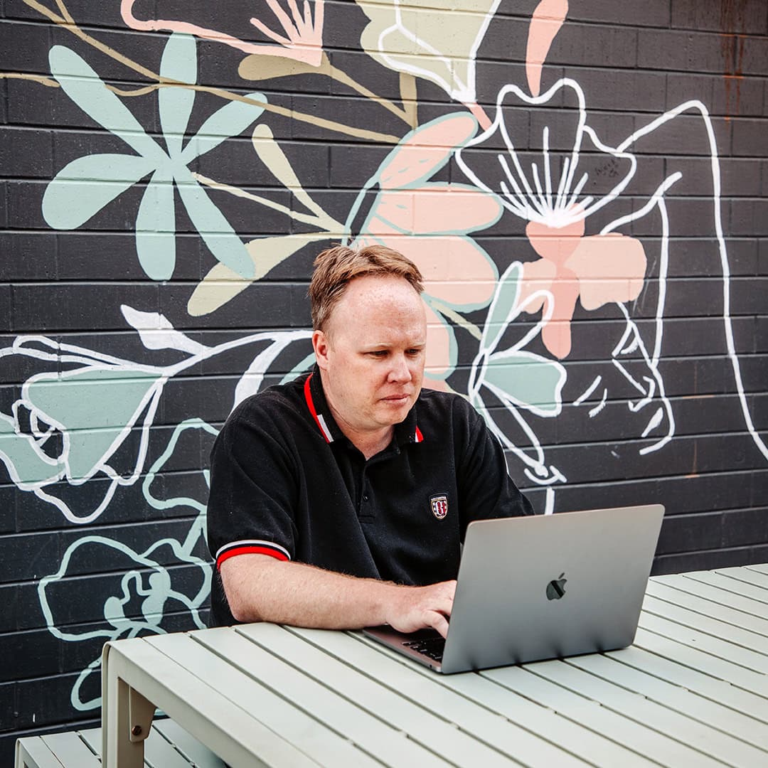 Man working on laptop at outdoor table with mural