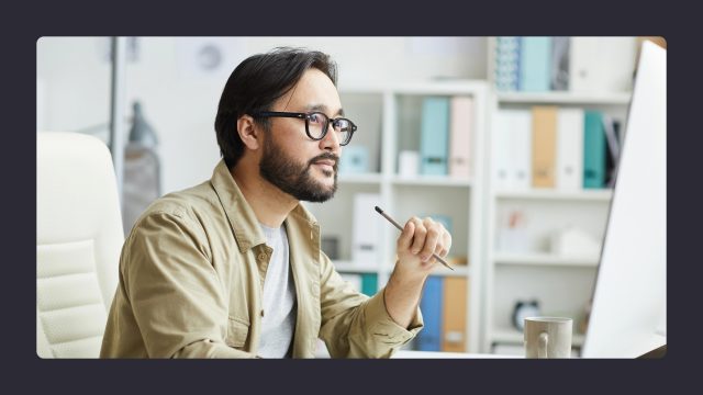 Man pondering at desk with computer, office background