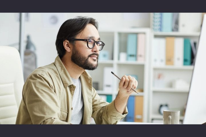 Man pondering at desk with computer, office background