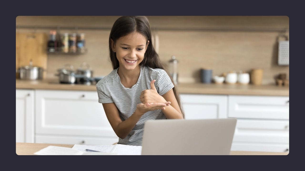 Young girl gesturing thumbs up at laptop in kitchen