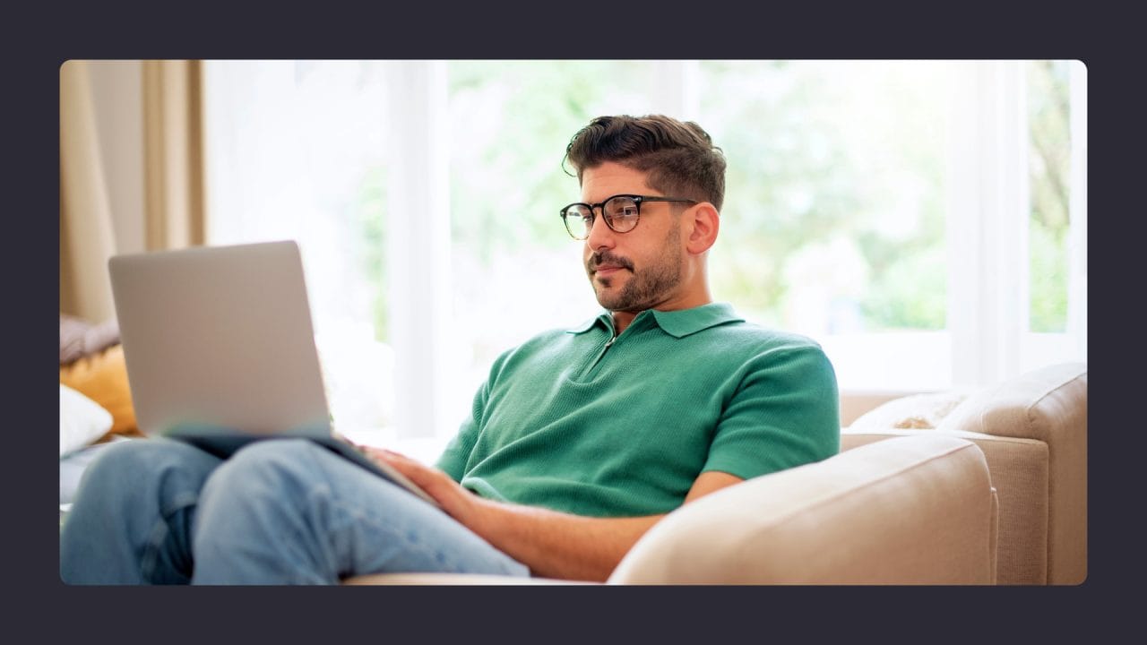 Man in green shirt using laptop on sunny couch