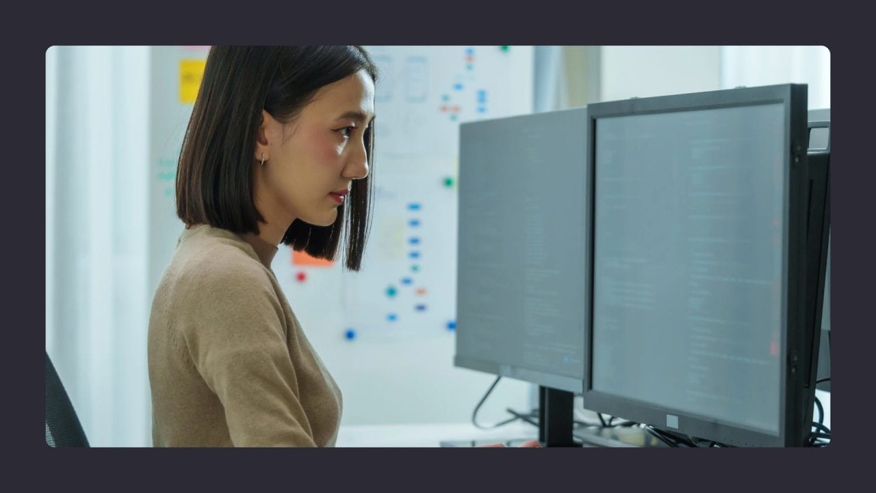 Woman focused on programming at dual monitors