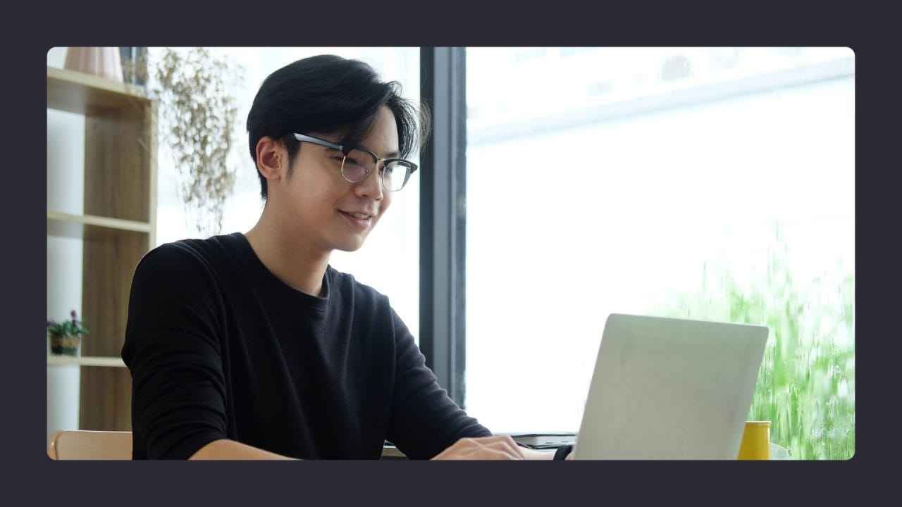 Young man smiling while working on laptop indoors