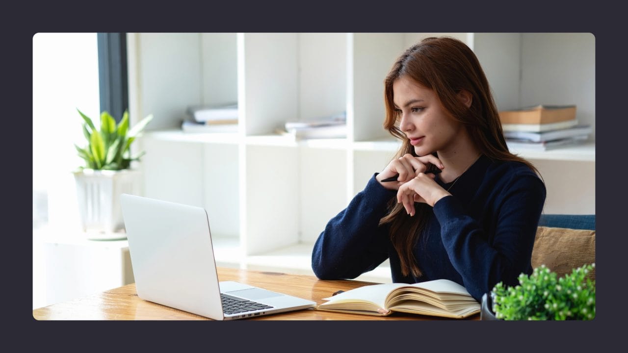 Woman pondering while working on laptop in bright office